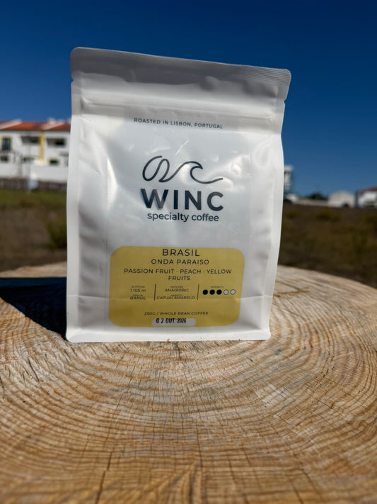 Saco branco de 250 g de café de especialidade Winc Onda Paraíso do Brasil, com rótulo amarelo, sobre uma superfície de madeira