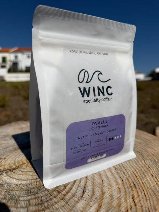 Saco branco de café Winc Ovalle da Guatemala, com rótulo lilás, sobre uma superfície de madeira